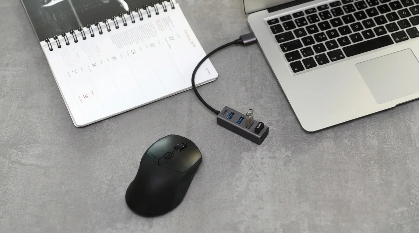 USB rozbočovač Yenkee YHB 4300 pripojený k notebooku na sivom stole vedľa čiernej myši a otvoreného zápisníka.
