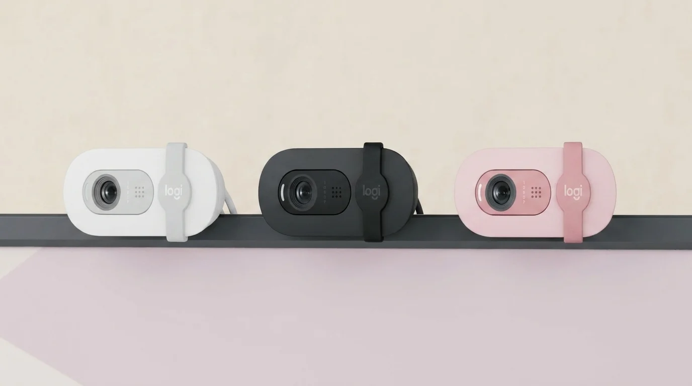 Tři webkamery Logitech Brio 100 v bílé, černé a růžové barvě připevněné na monitoru.