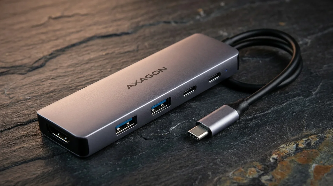 Sivý hliníkový USB hub AXAGON s káblom USB-C a portami HDMI, USB-A a USB-C na tmavom kamennom povrchu.