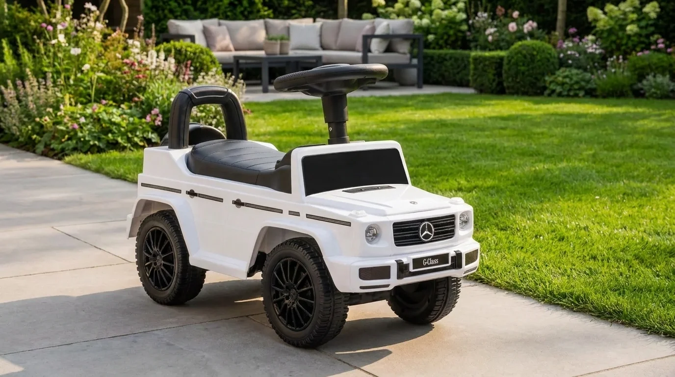 Bílé dětské odrážedlo Buddy Toys Mercedes-Benz G350d s černým sedadlem a volantem zaparkované na dlážděné terase u zahrady.