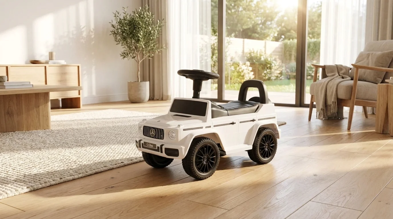 Bílé dětské odrážedlo Buddy Toys Mercedes-Benz G350d s černým volantem a sedátkem stojí na dřevěné podlaze ve světlém obývacím pokoji.