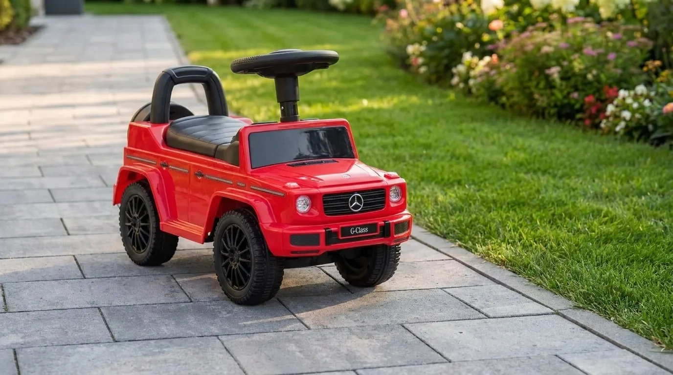 Červené dětské odrážedlo Buddy Toys Mercedes G350d stojící na dlážděném chodníku v zahradě vedle trávníku.