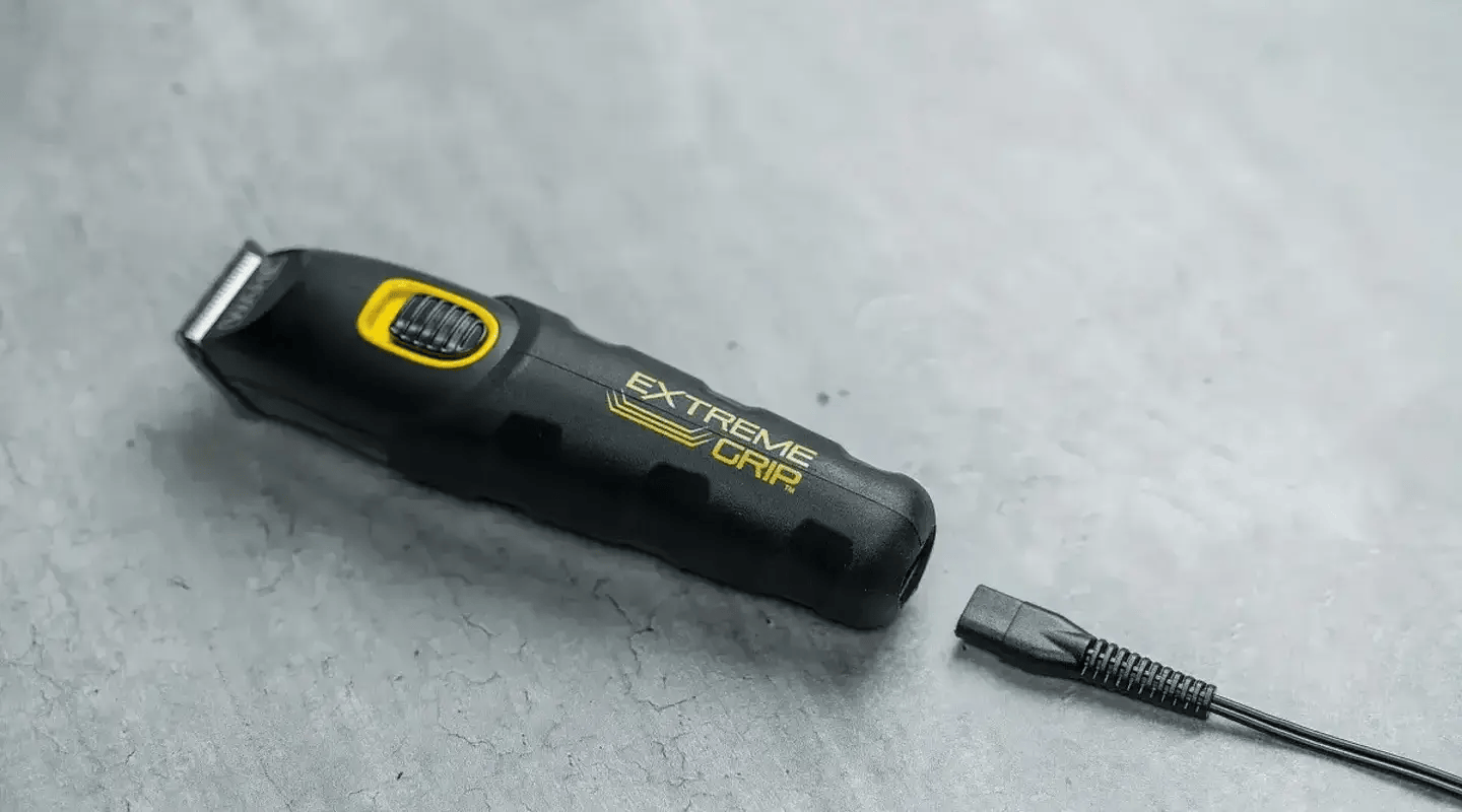Čierny multifunkčný zastrihávač Wahl Extreme Grip so žltými detailmi leží na sivom podklade vedľa nabíjacieho kábla.