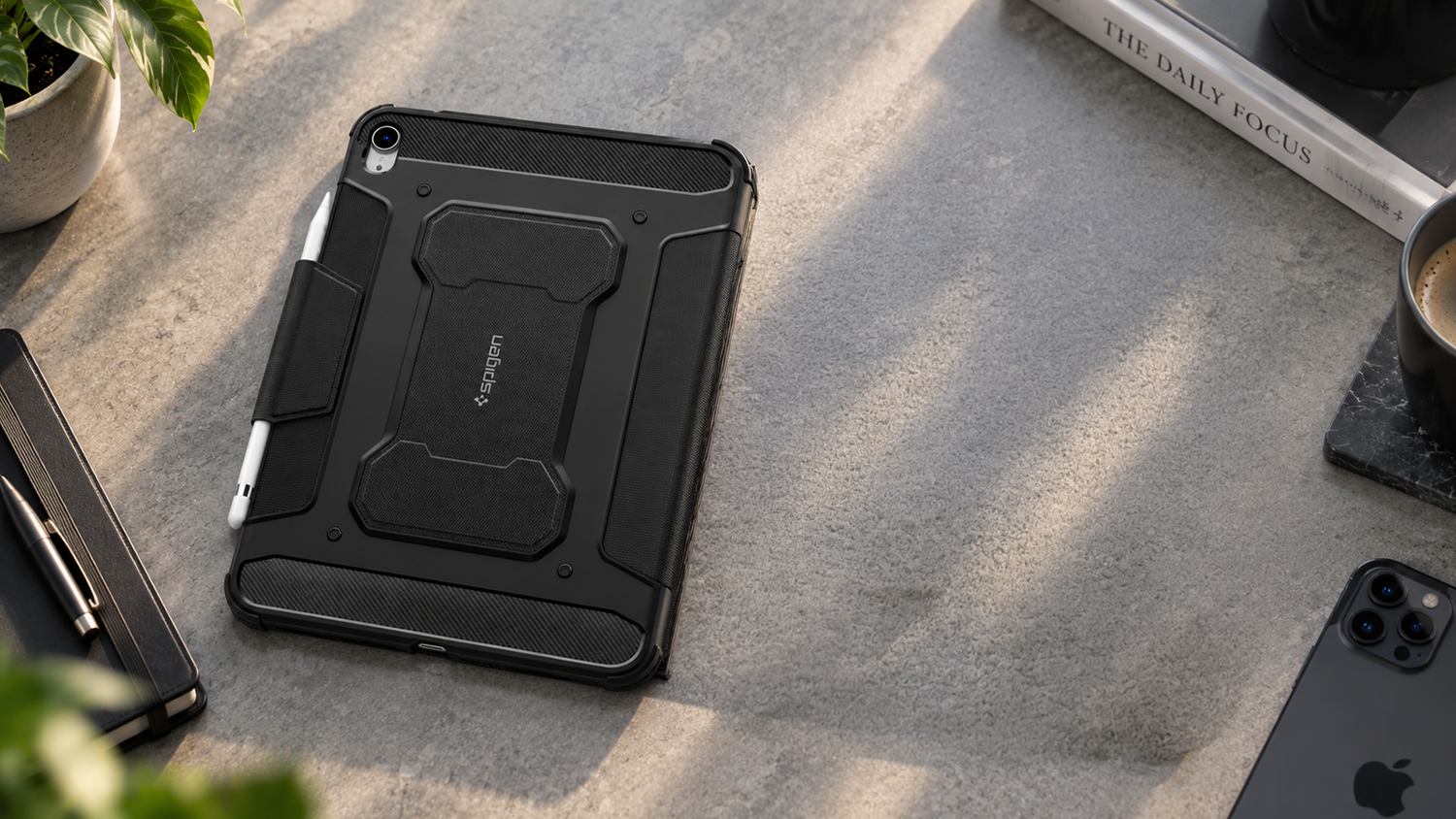 Černé pouzdro Spigen Rugged Armor Pro na iPad s uchyceným stylusem položené na kamenném stole.