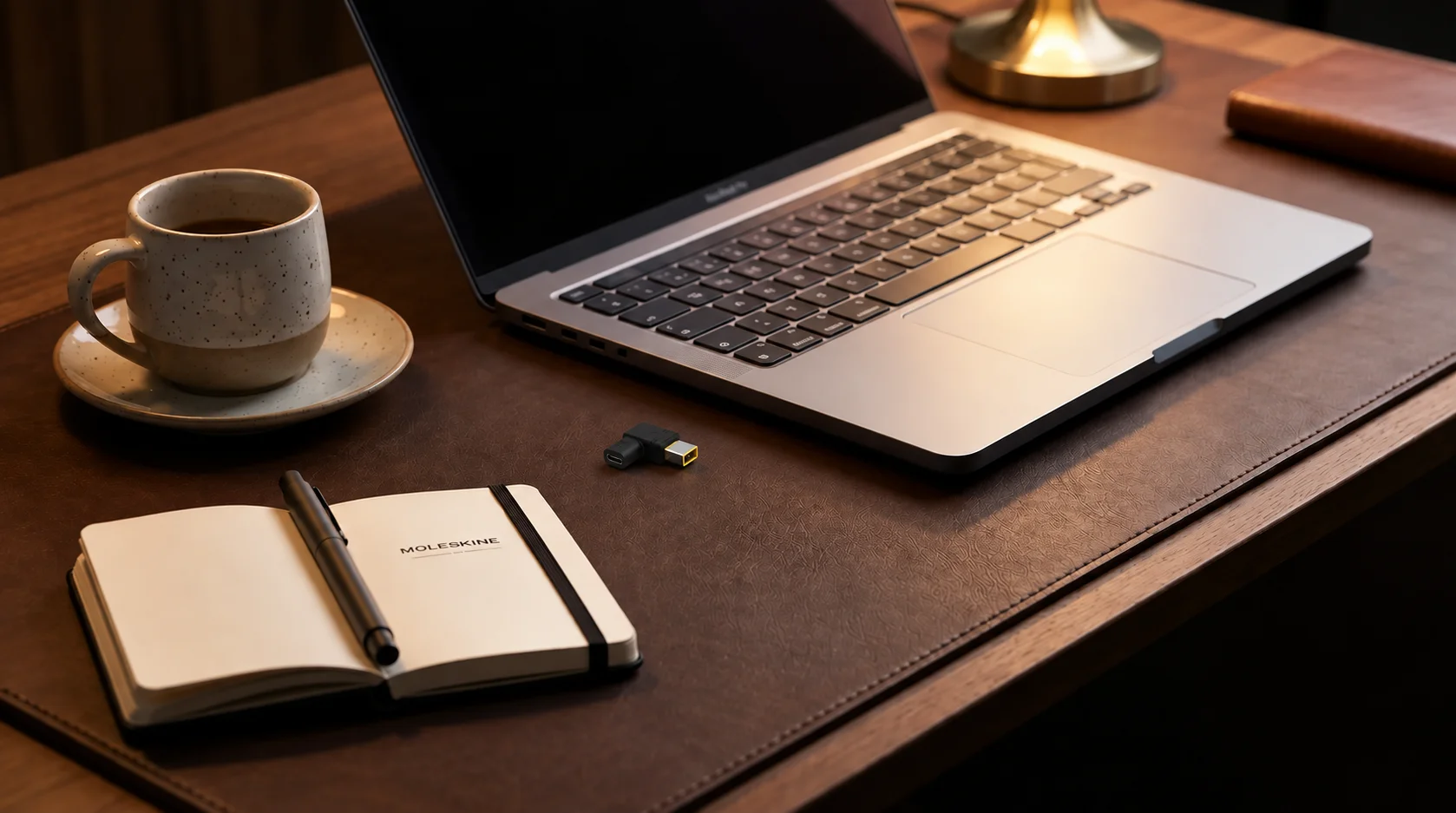 Napájecí redukce Aligator USB-C na hnědé kožené podložce vedle notebooku, otevřeného zápisníku a šálku kávy.