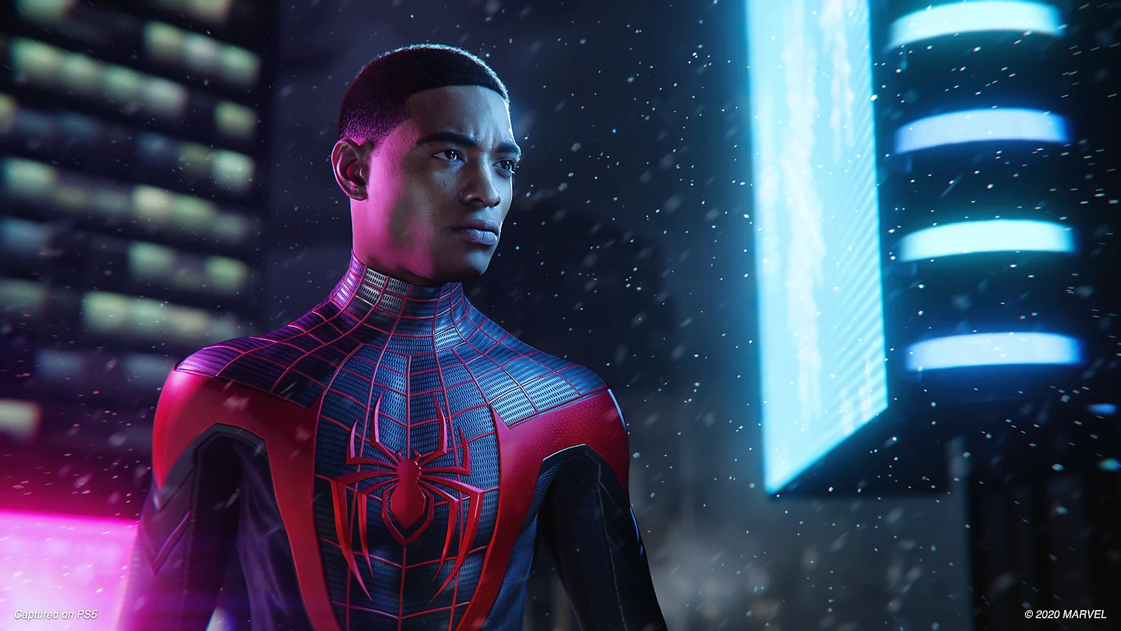 Miles Morales bez masky v čierno-červenom obleku Spider-Mana hľadí do strany v zasneženom meste s jasnými neónovými svetlami.