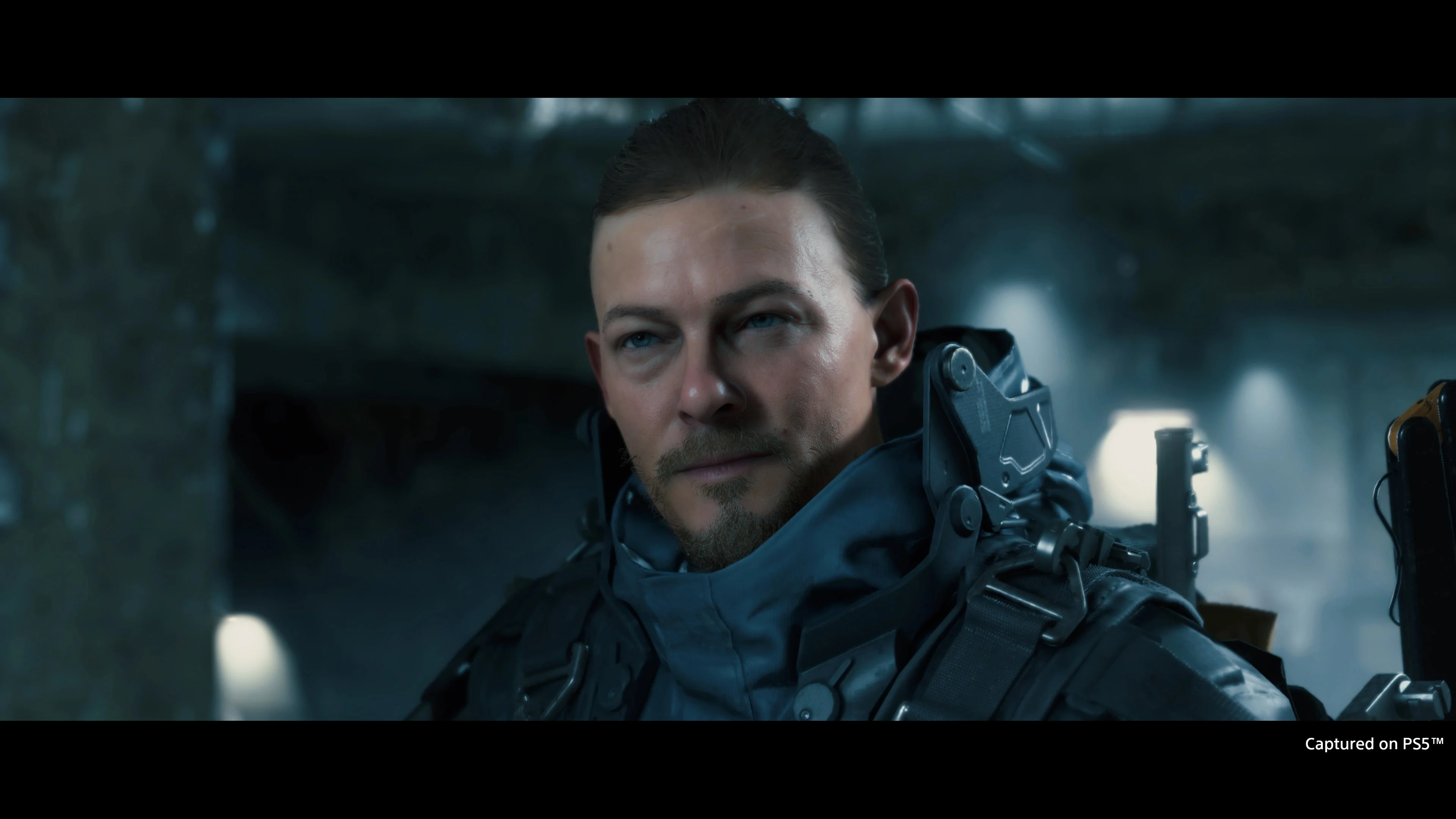 Detailní záběr na hlavního hrdinu Sama Bridgese ze hry Death Stranding ve futuristickém obleku.