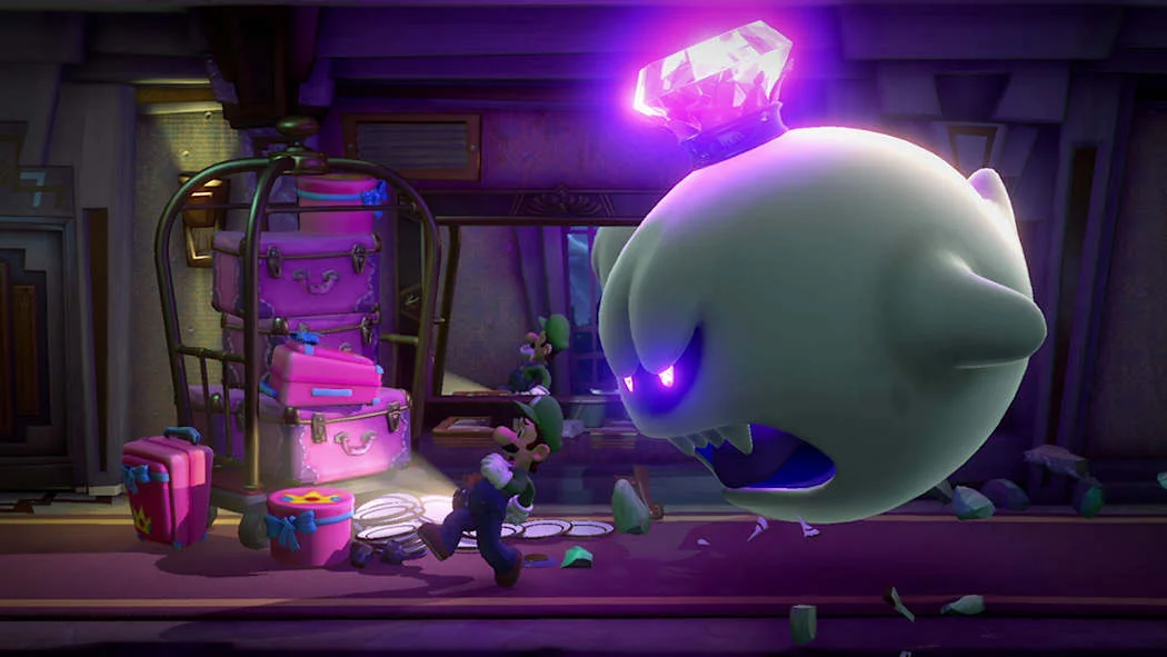 Luigi vyděšeně utíká před obřím duchem King Boo s fialově zářící korunou v hotelové chodbě s růžovými kufry.