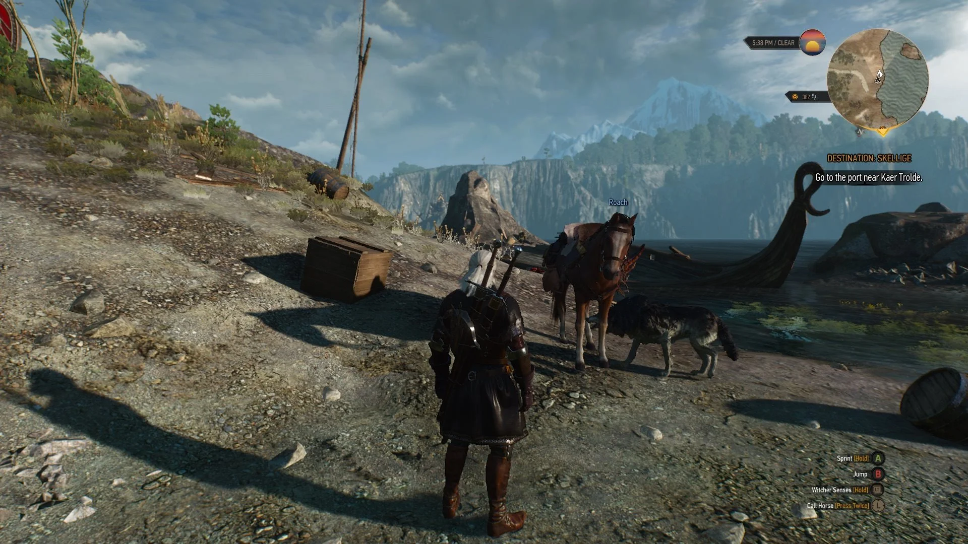 Geralt z Rivie stojí na kamenitém pobřeží vedle svého koně a lodi s výhledem na zasněžené hory v pozadí ve hře Zaklínač 3: Divoký Hon.