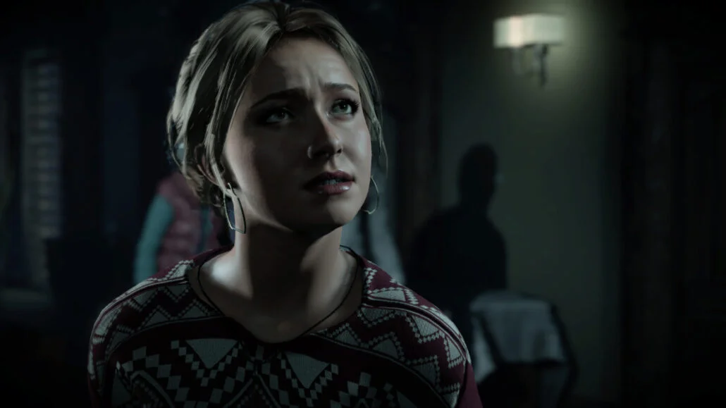 Mladá žena s blonďatými vlasy a ustaraným výrazem v tmavém interiéru ze hry Until Dawn.