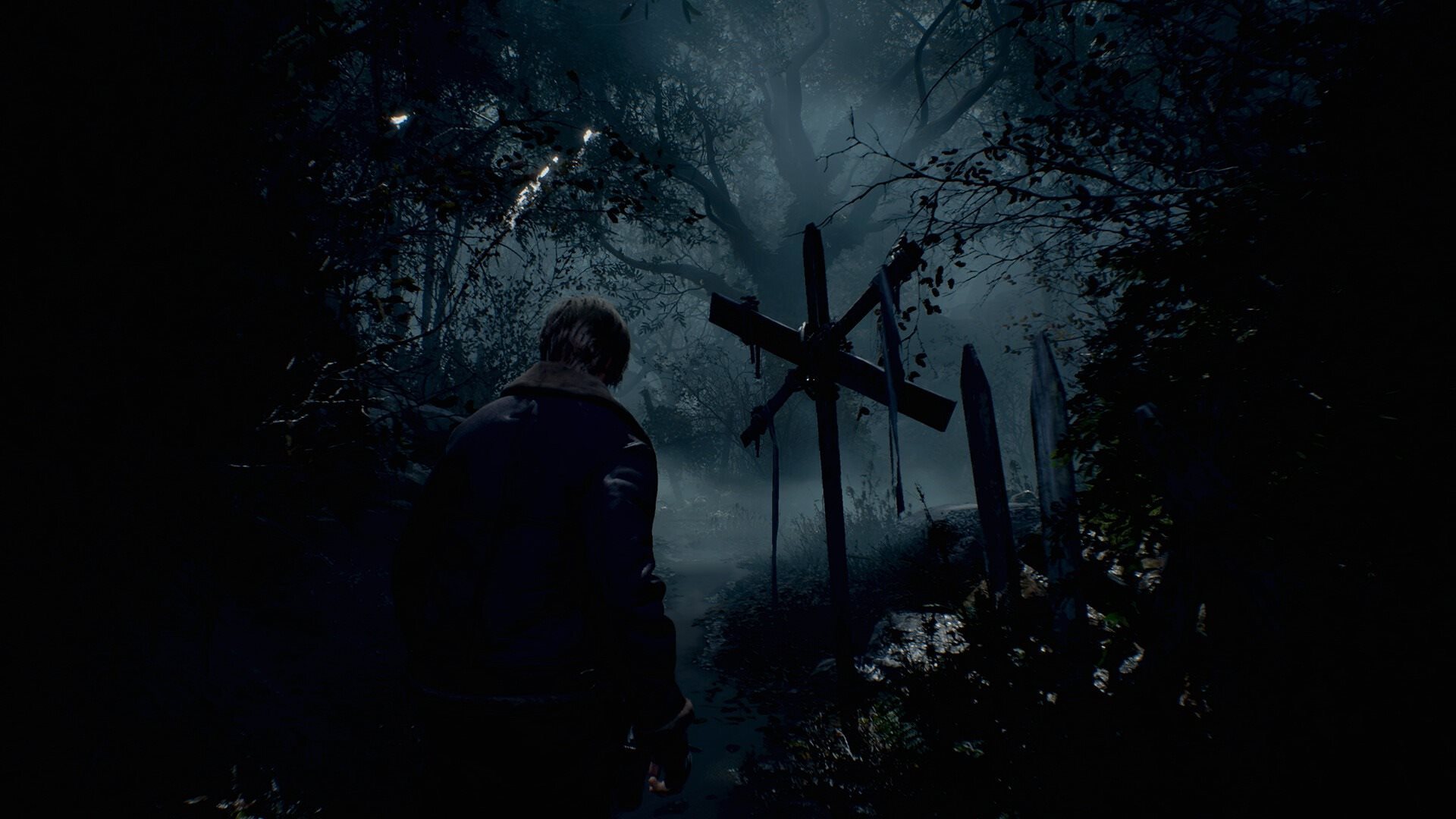 Leon S. Kennedy stojí zády v temném a mlhavém lese před dřevěným křížem ve hře Resident Evil 4.