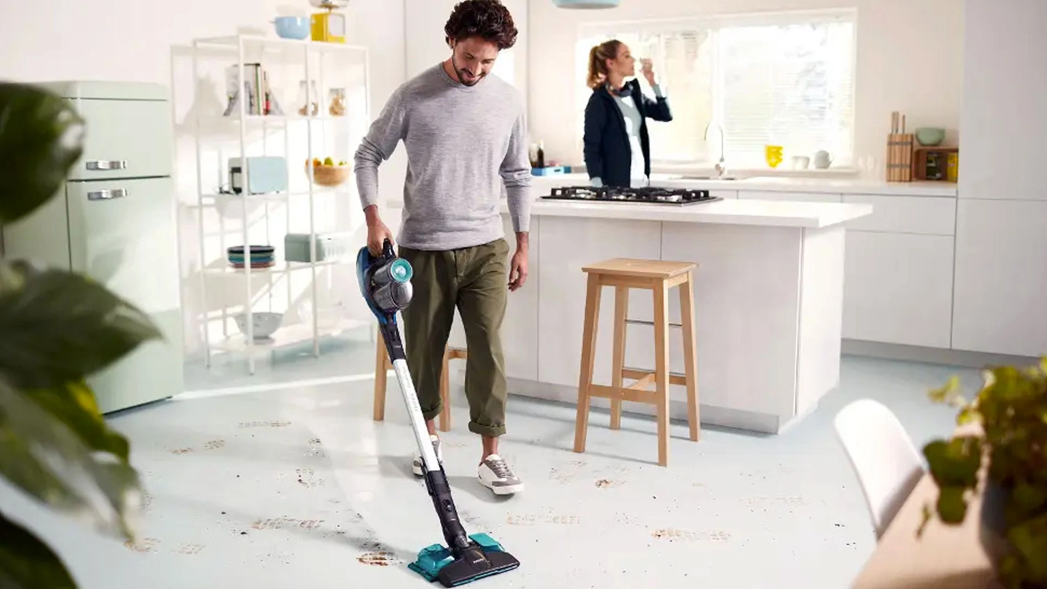Muž vysává špinavé stopy na podlaze v kuchyni pomocí tyčového vysavače Philips SpeedPro.
