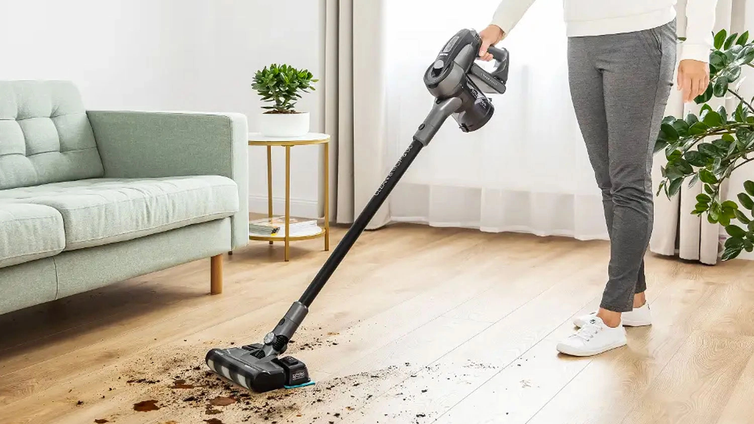 Osoba uklízí nečistoty na dřevěné podlaze pomocí tyčového vysavače Sencor s mopovacím nástavcem.