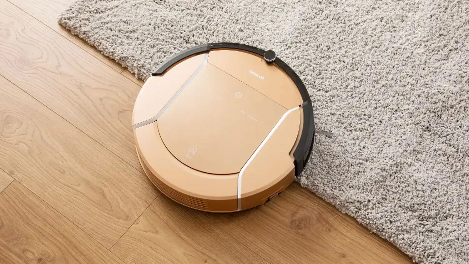 Zlatý robotický vysávač Sencor na drevenej podlahe prechádza na svetlý koberec.