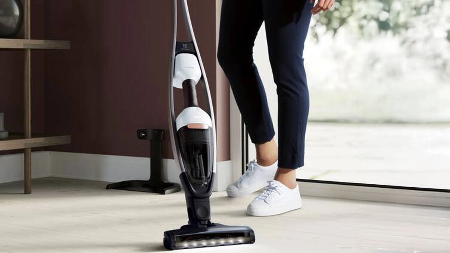 Tyčový vysavač Electrolux Pure Q9 stojící na světlé podlaze vedle osoby v bílých teniskách.