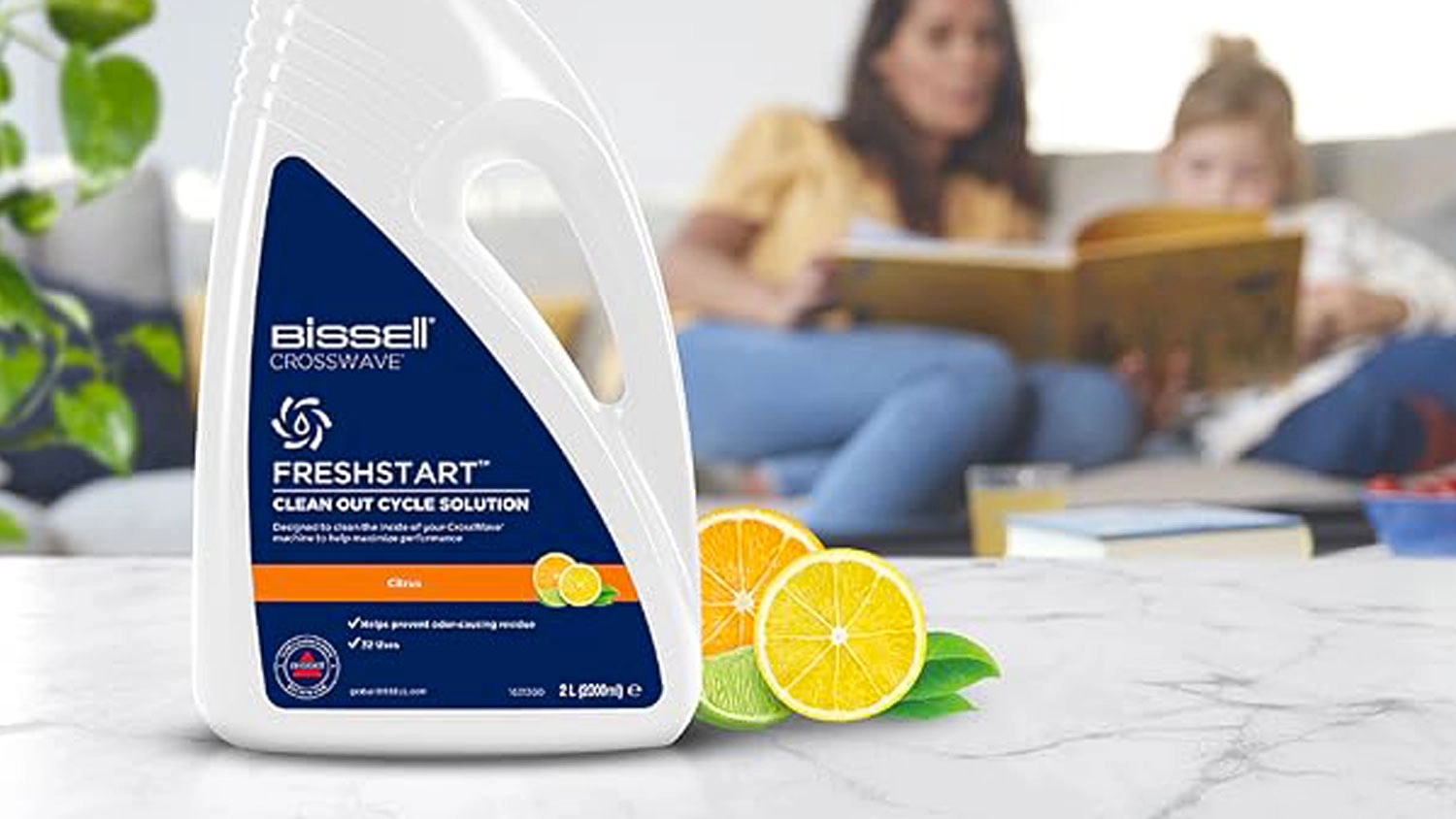 Čistiaci prostriedok BISSELL Crosswave FreshStart s plátkami citrusov na mramorovom povrchu a rozmazanou rodinou v pozadí.