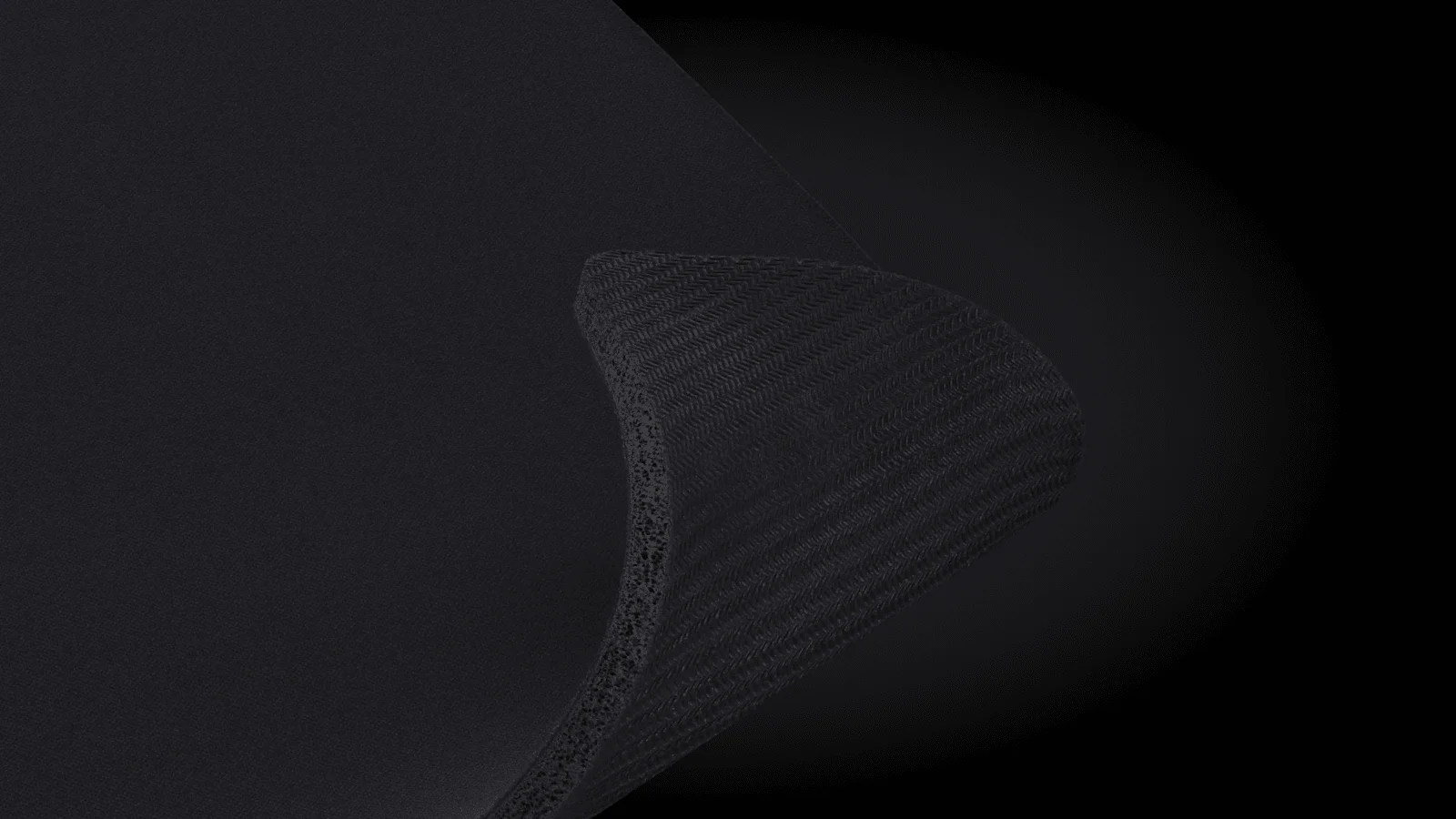 Detail ohnutého rohu černé podložky Logitech G740 L s pohledem na její tloušťku a texturovanou protiskluzovou pryžovou základnu.