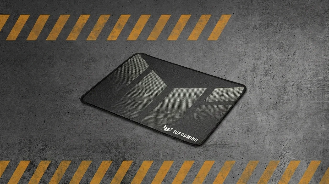 Čierna herná podložka pod myš ASUS TUF Gaming P1 na sivom betónovom pozadí s výstražnými pruhmi.