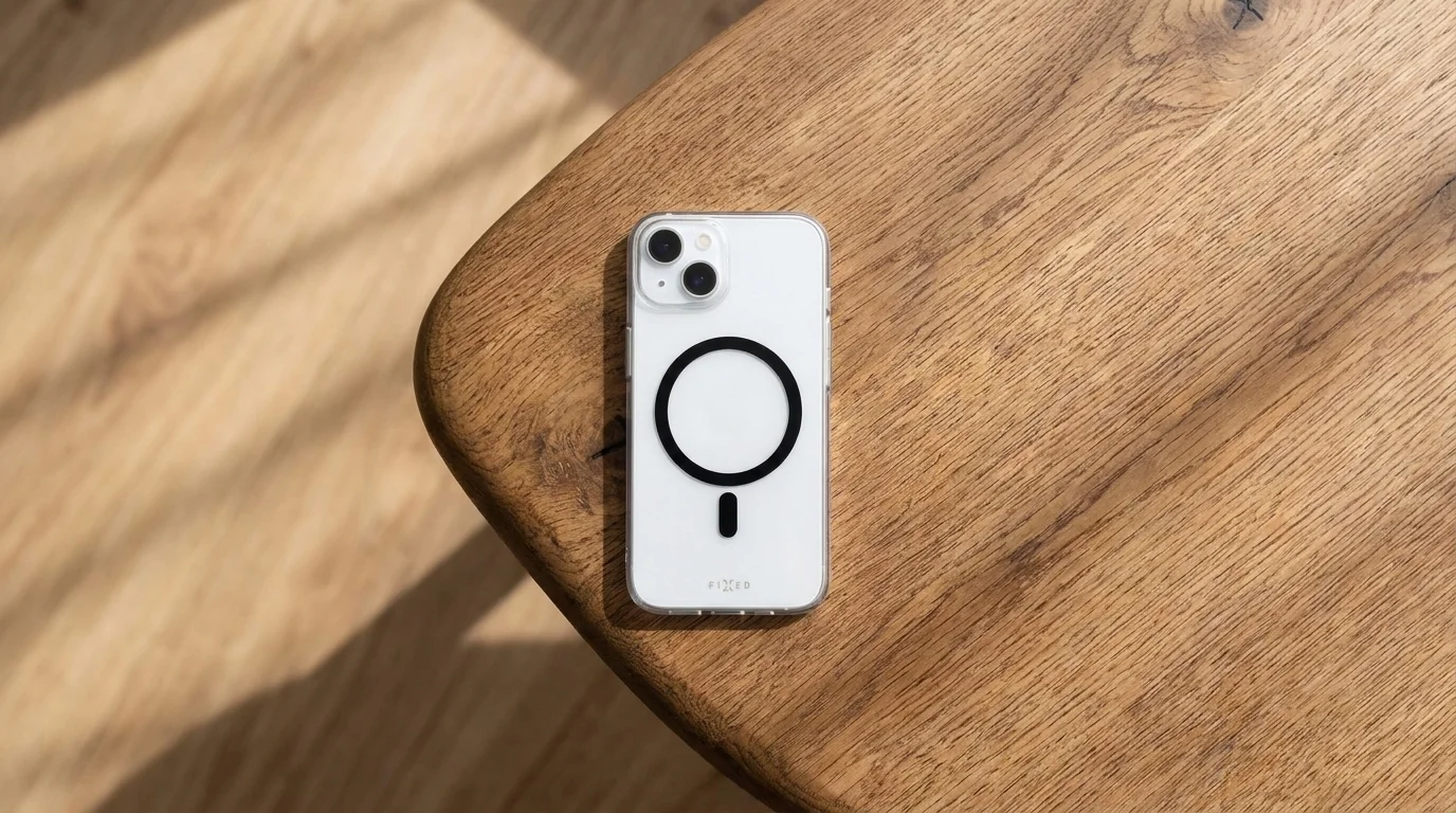 Bílý iPhone v průhledném krytu FIXED MagPurity s černým MagSafe kroužkem položený na dřevěném stole.