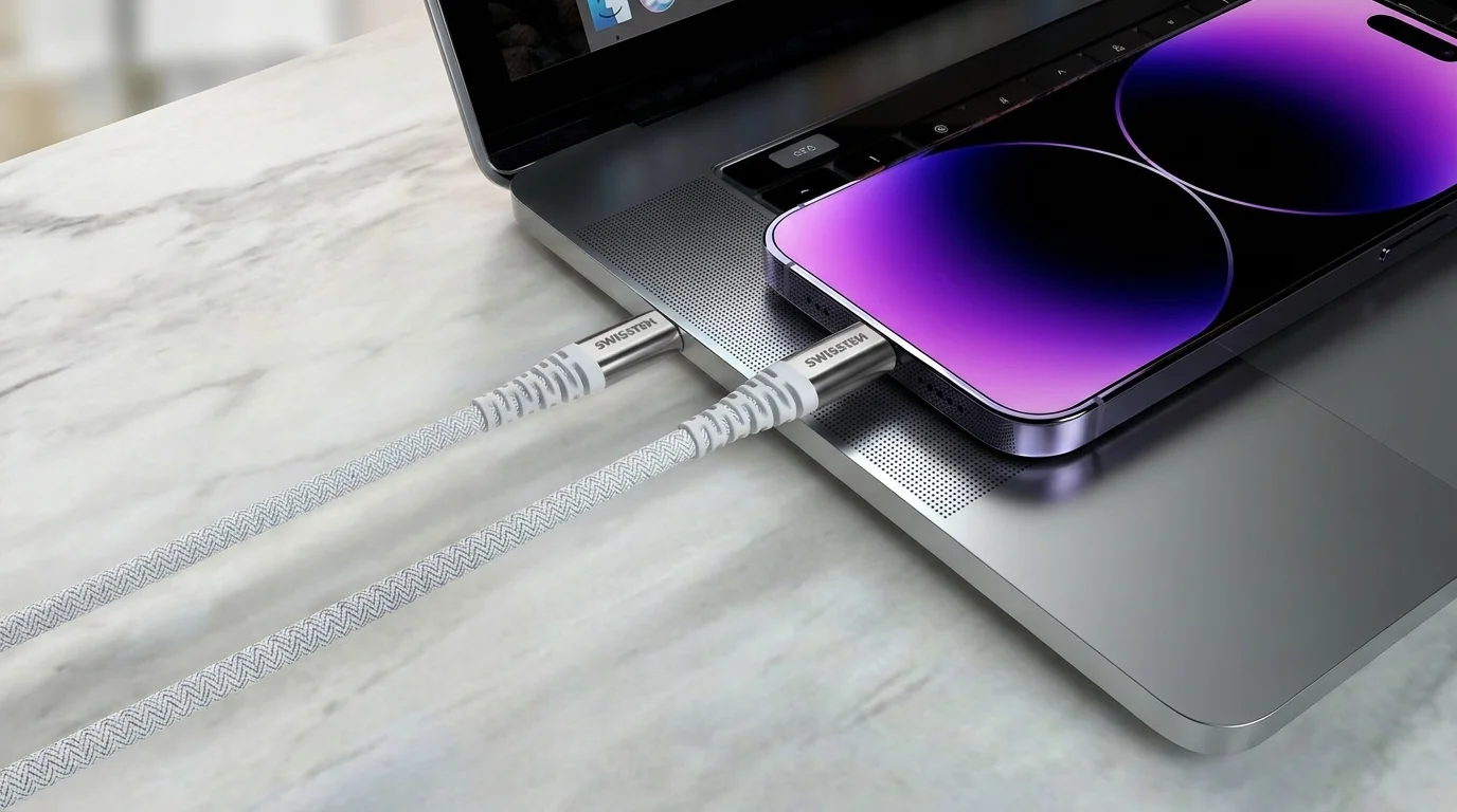 Bílý opletený kabel Swissten zapojený do notebooku a smartphonu položeného na jeho těle.