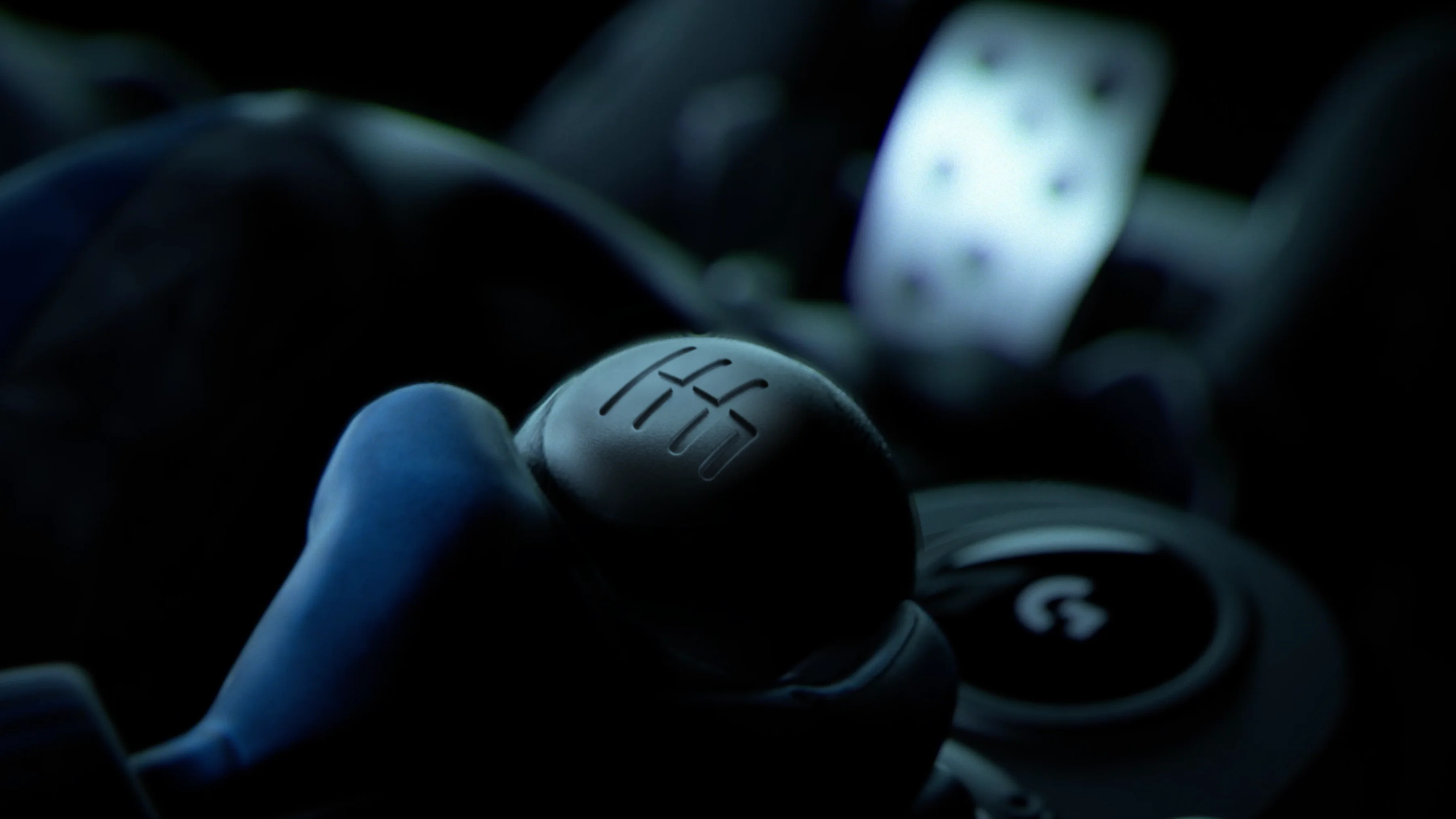 Detailní záběr na hlavici řadicí páky Logitech Driving Force Shifter s vyrytým schématem řazení v tmavém prostředí.