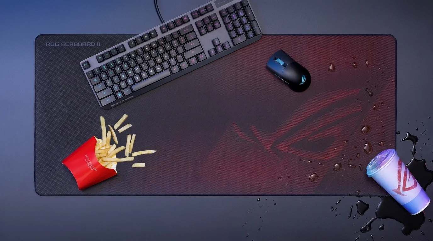 Herní podložka Asus ROG Scabbard II s položenou klávesnicí, myší, hranolky a kapkami vody z rozlitého nápoje.