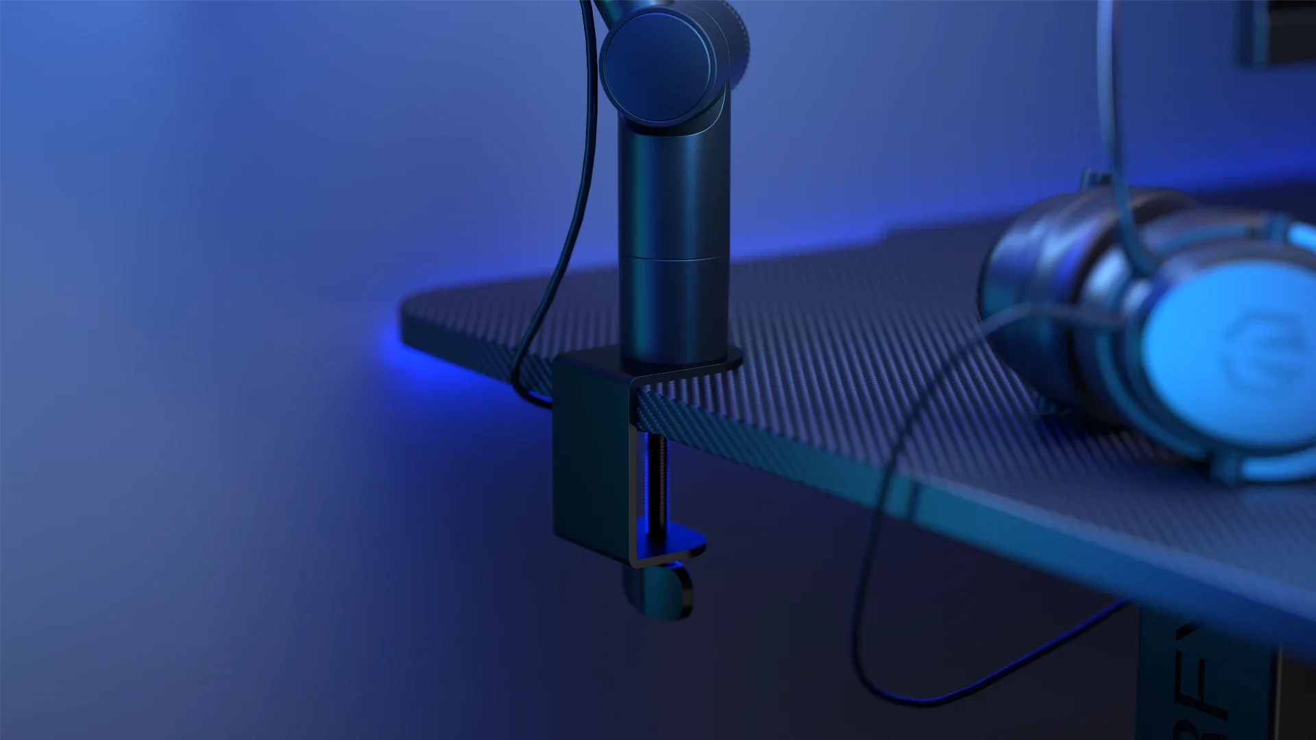 Stolní úchyt mikrofonního stojanu ENDORFY Studio Boom Arm Black připevněný k desce stolu s karbonovou texturou a modrým osvětlením.