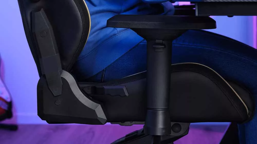 Detail nastaviteľnej lakťovej opierky a bočného mechanizmu hernej stoličky Trust GXT 721 Ruya so sediacou osobou.