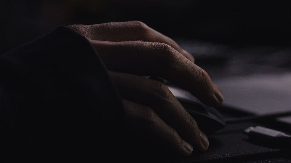 Detail ruky držiacej hernú myš na podložke v tmavom prostredí.