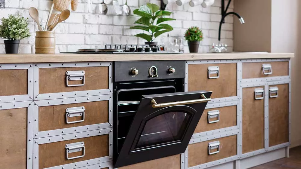 Čierna vstavaná rúra Electrolux v retro dizajne s pootvorenými dvierkami a mosadzným madlom v rustikálnej kuchynskej linke.