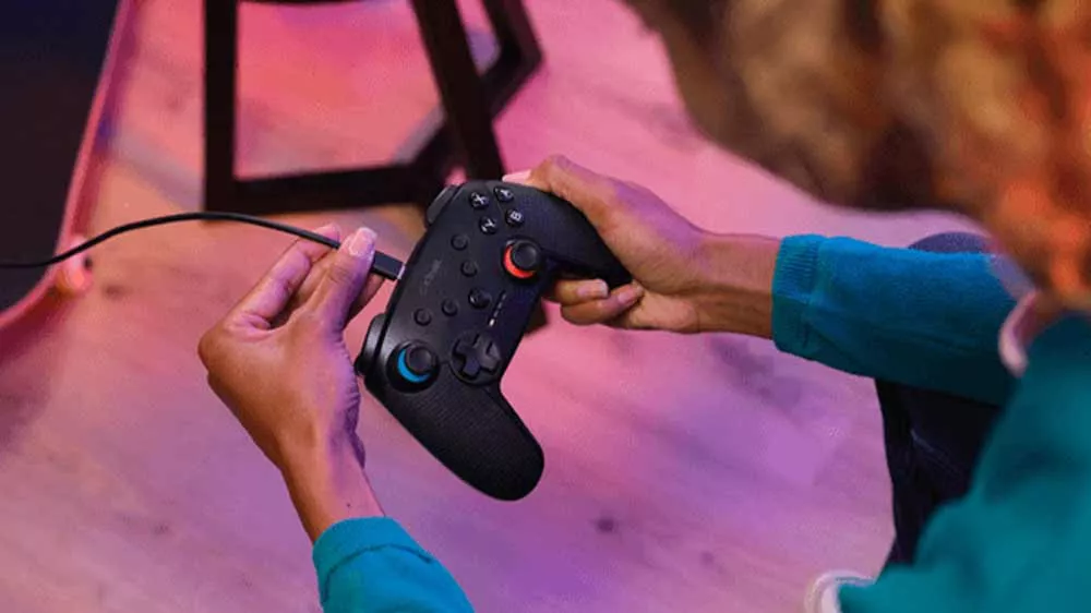 Hráč drží čierny gamepad Trust GXT 1246 Muta a zapája doň nabíjací kábel.