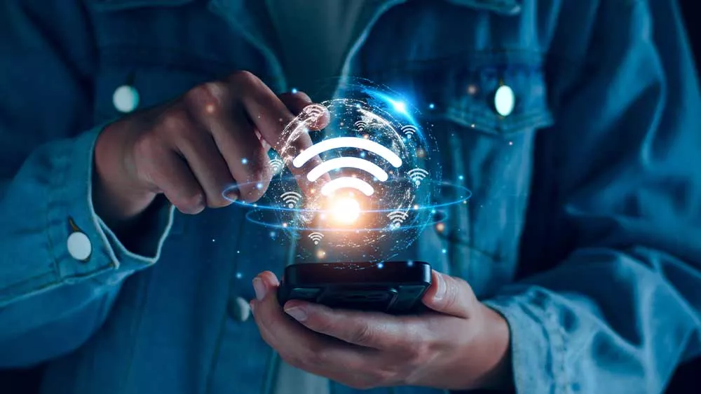 Osoba drží smartfón, nad ktorým sa vznáša žiariaci grafický symbol Wi-Fi siete.