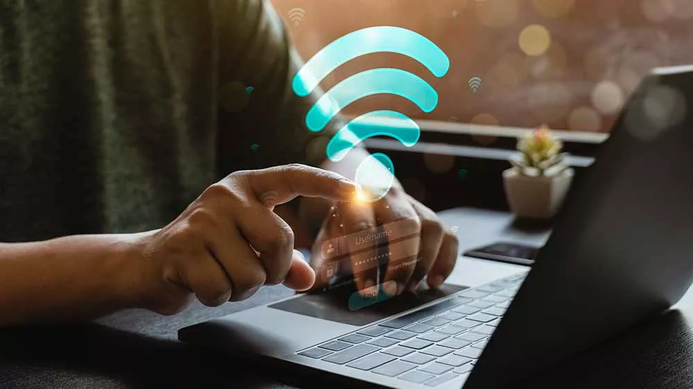 Ruky na klávesnici notebooku s grafickým symbolom Wi-Fi a prihlasovacím formulárom.