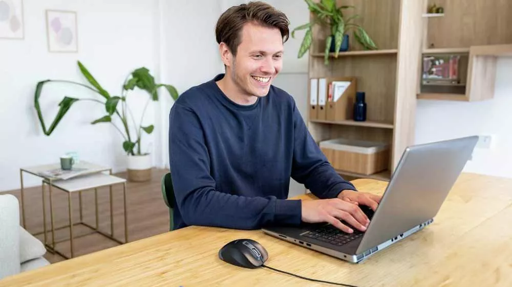 Usmievavý muž pracuje na notebooku pri stole s pripojenou drôtovou myšou Trust Fyda Eco.