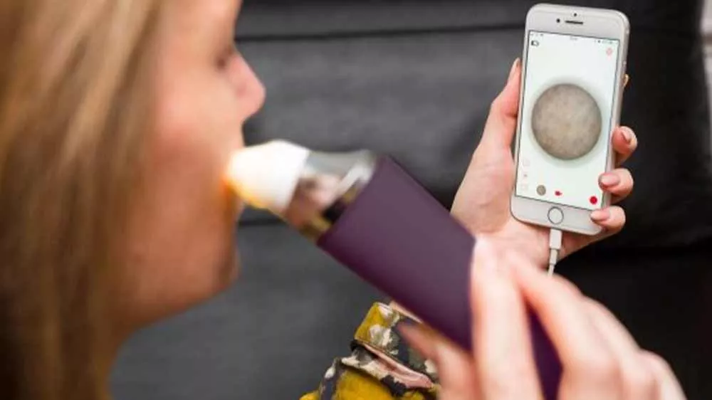 Žena používa mikrodermabráziu Rio DRMC na tvári a sleduje zväčšený záber pleti na pripojenom smartfóne.