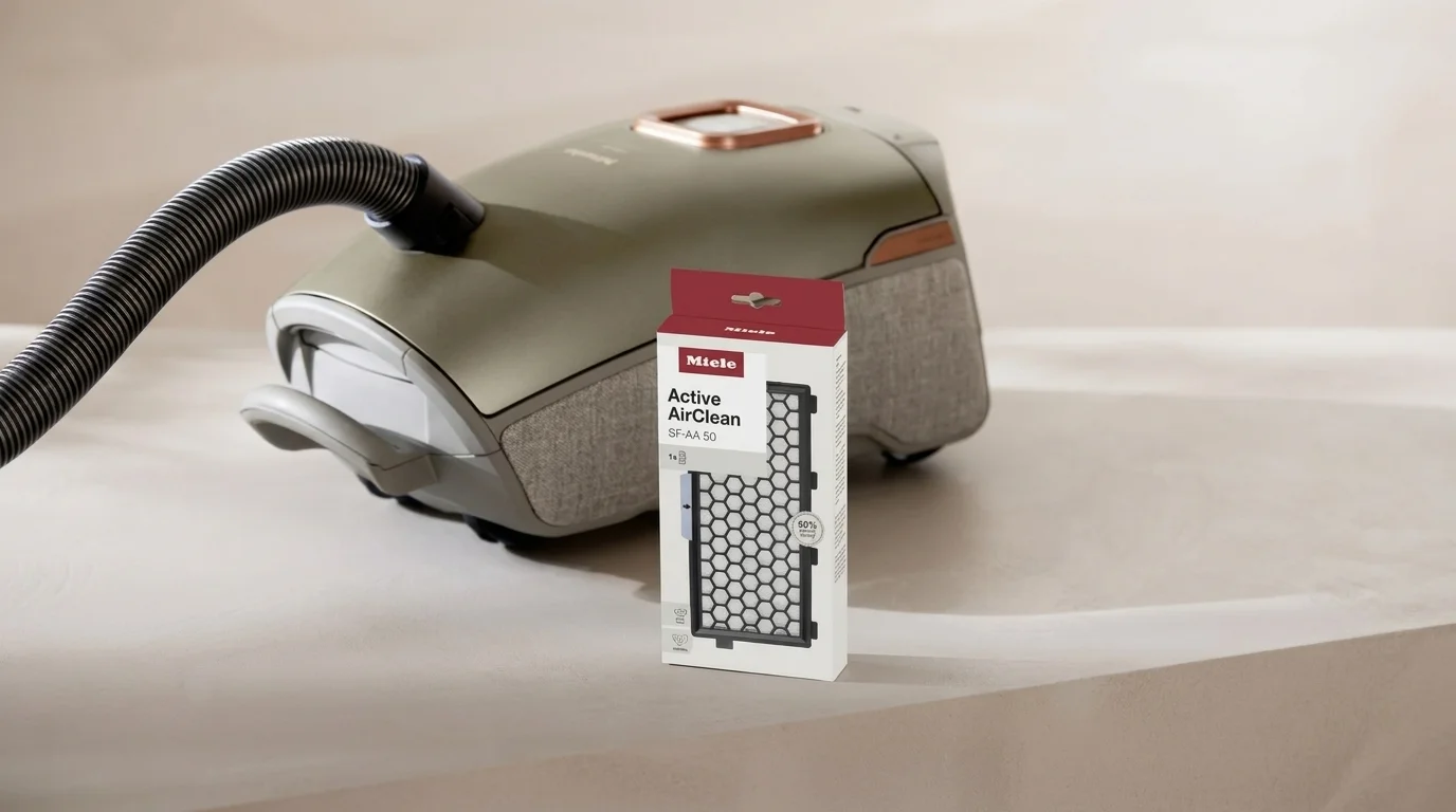 Balení náhradního filtru Miele Active AirClean SF-AA 50 postavené před podlahovým vysavačem Miele.
